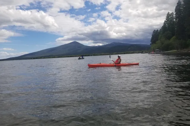 A kayaker on a calm lake with a forested mountain behind