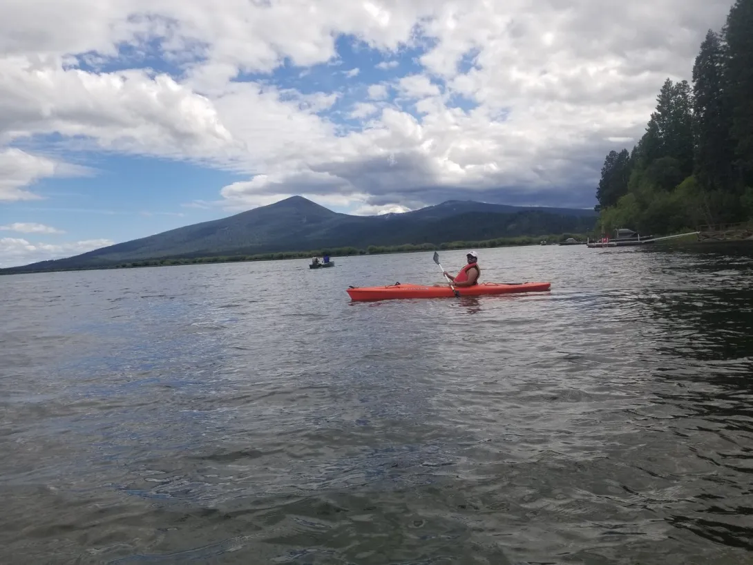 A kayaker on a calm lake with a forested mountain behind